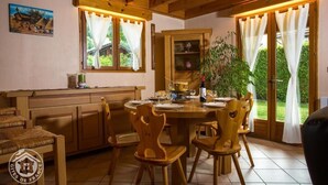 A wooden dining area with a round table and chairs, a cabinet with glass doors, and a window with curtains.