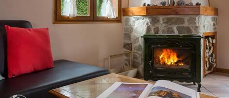A cozy room with a stone fireplace, a black leather sofa with a red pillow, and a wooden table with an open book.