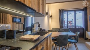 A modern kitchen with wooden accents, a dining area with a table and chairs, and a view of the outside through large windows. - ROND-POINT DES PISTES - INTERLUDE (TIGNES)