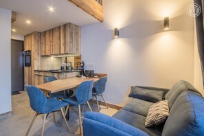 A modern kitchen with wooden cabinetry, a dining table with chairs, and a sofa with cushions.