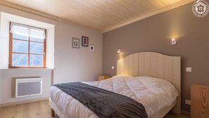 A bedroom with a large bed, a window with a view, a radiator, and a wall-mounted light. - LE PRESBYTERE 5 - MONTSAPEY (MONTSAPEY)