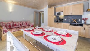 A modern kitchen with wooden cabinets, a microwave, and a dishwasher. There is a dining area with a table set for four, red placemats, and a red and white patterned sofa. - LE PRESBYTERE 5 - MONTSAPEY (MONTSAPEY)