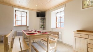 A dining area with a wooden table set for four, benches, a TV mounted on the wall, and a window with a view. - LE PRESBYTERE 5 - MONTSAPEY (MONTSAPEY)