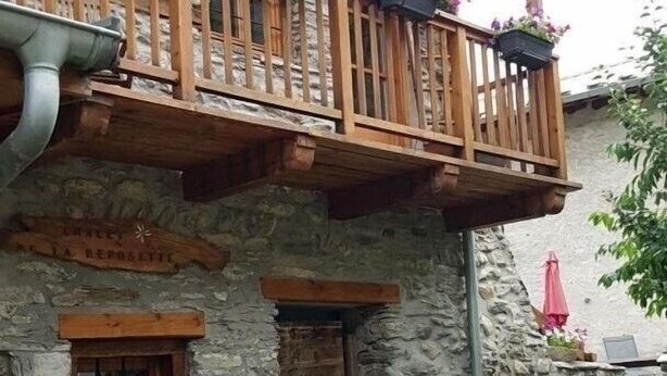 A stone building with a wooden balcony, a small window, and a stone pathway leading to a bench. - LE BOUQUETIN - VAL CENIS (VAL CENIS)