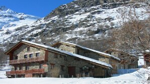 A stone building with a wooden balcony, set against a snowy mountain backdrop. - LES COLOMBIERES - MÉSANGE (BONNEVAL SUR ARC)