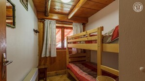 A small, cozy room with wooden bunk beds, a window with red curtains, and a radiator on the floor. - LES COLOMBIERES - MÉSANGE (BONNEVAL SUR ARC)