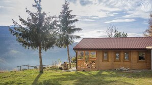 Une cabane en bois avec un toit recouvert de tuiles rouges, une véranda et une vue sur un lac et des montagnes.