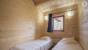 Une chambre dans un chalet en bois, avec deux lits, une fenêtre avec des rideaux et un luminaire au plafond.