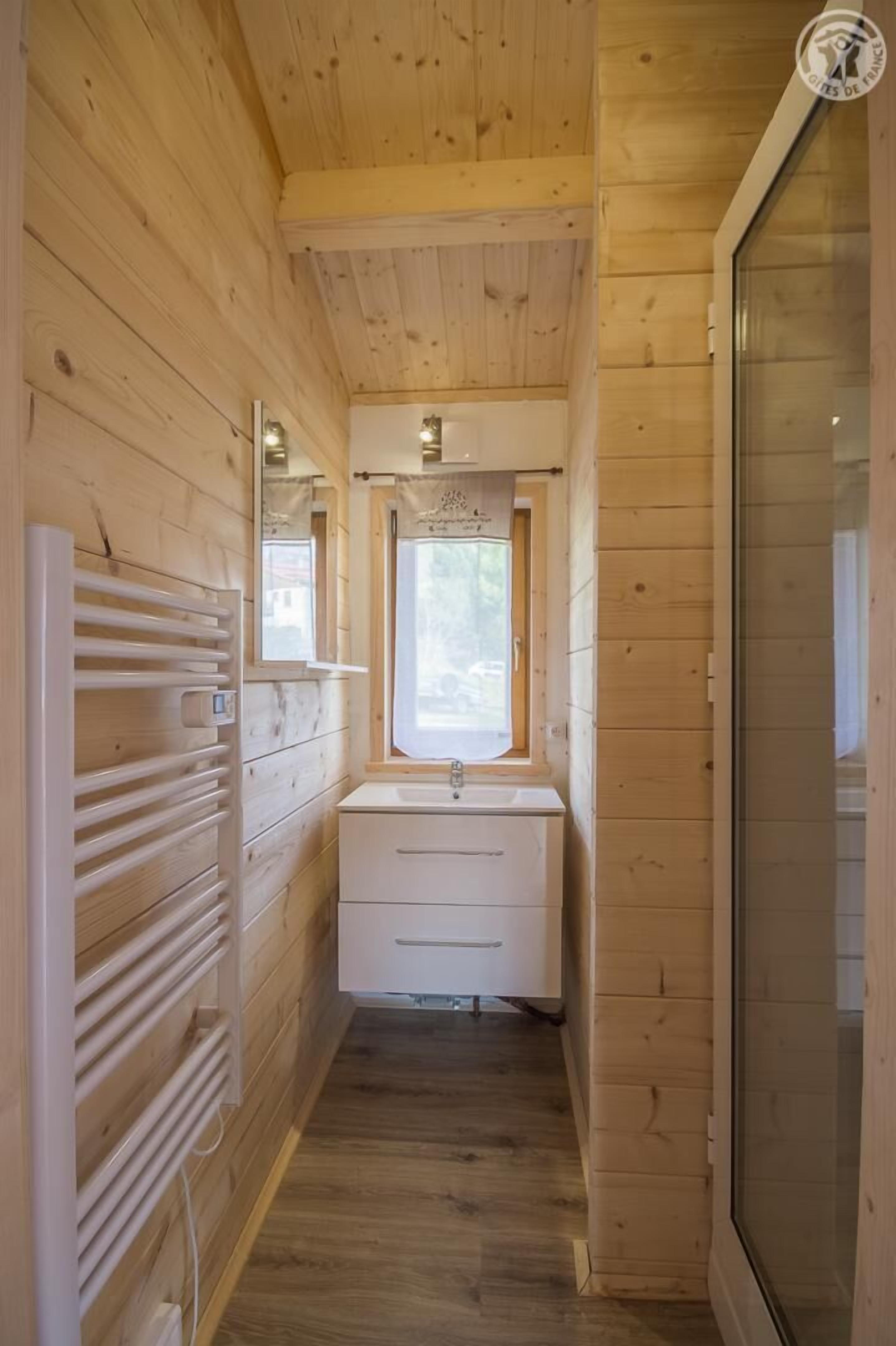 Een smalle houten gang met een radiator, een raam en een wastafel.