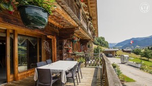 A wooden outdoor dining area with a table and chairs, a hanging planter, and a view of the mountains. - LA FERME D'EUGENIE - FLUMET (FLUMET)