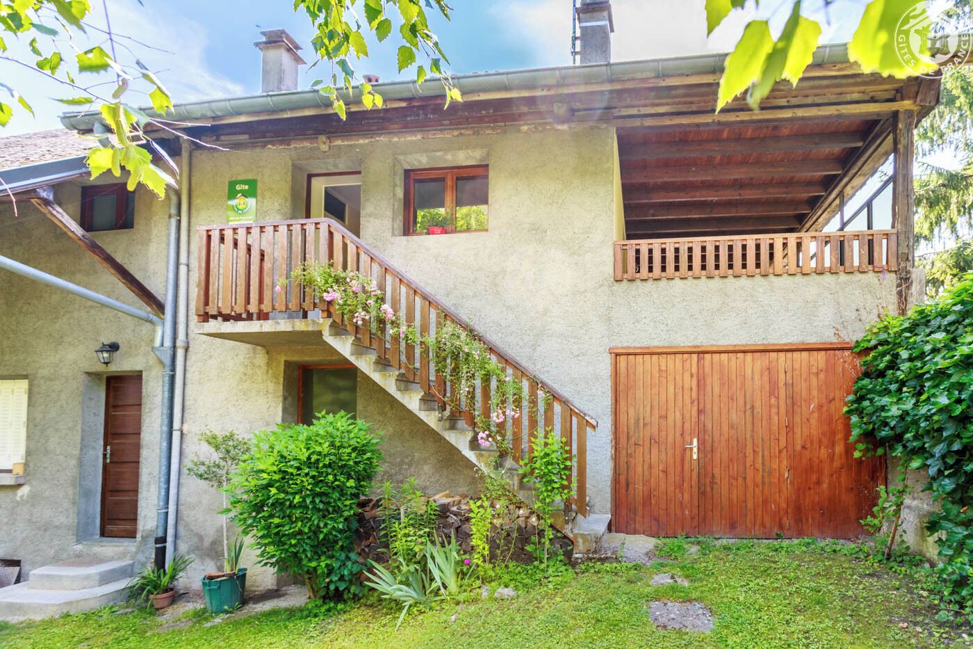 A two-story house with a wooden staircase, a wooden gate, and a small garden area.