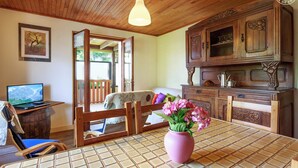 Ein gemütlicher Raum mit Holzbalkendecke, einem Esstisch mit einer rosa Vase, einem Laptop auf einem Holzfass und einem Holzschrank mit dekorativen Schnitzereien.