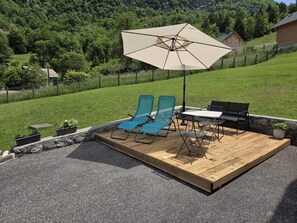 Un terrazzo in legno con mobili da esterno, tra cui due poltrone blu, un tavolo e un ombrellone grande.