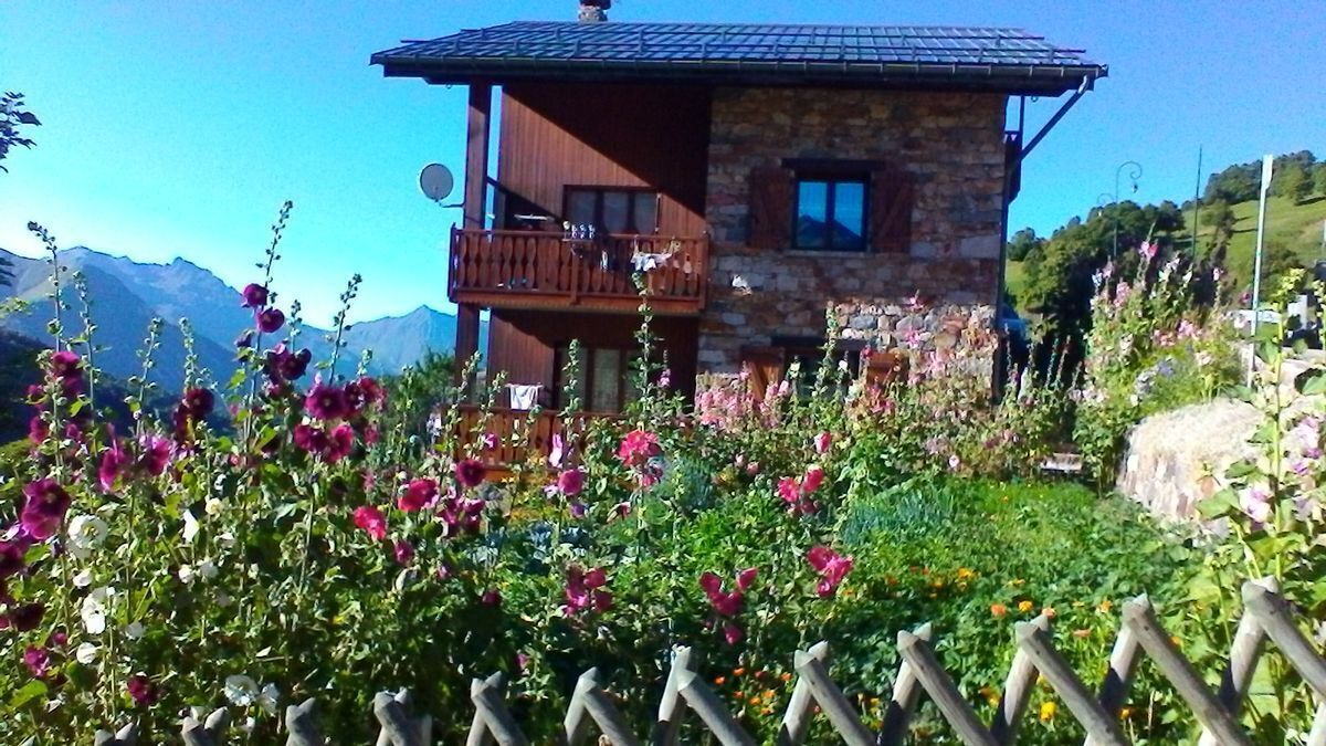 Un bâtiment en pierre de deux étages, doté d’un balcon et entouré d’un jardin où poussent différentes sortes de fleurs.