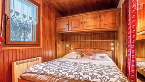 Una habitació de fusta amb un llit, una finestra amb decoracions en forma de cor i un llit superposat.