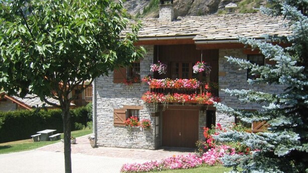 Una casa de pedra amb una porta de fusta i un balcó ple de cistells de flors penjants.