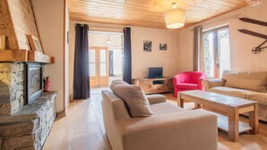 Una sala de estar acogedora con chimenea de piedra, un sillón rojo, un sofá beige y una mesa de centro de madera.