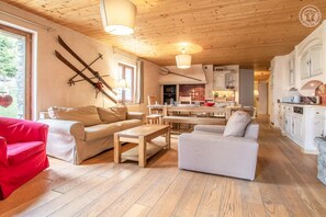 Un salon chaleureux avec un canapé, un fauteuil rouge et une table basse en bois. On y trouve également un coin cuisine avec des meubles blancs et une table à manger.