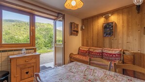 A cozy room with a wooden bench, a bed with a patterned bedspread, a wooden dresser, and a large window offering a view of a forested area. - LA BERTINA - MERIBEL LES ALLUES (MERIBEL LES ALLUES)