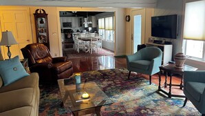 A living room with a brown leather sofa, a blue armchair, and a glass coffee table. There is a colorful rug on the floor, and a wooden ceiling with exposed beams. - Stunning Lakefront Escape! Book Your Dream Getaway! (Woodstock)