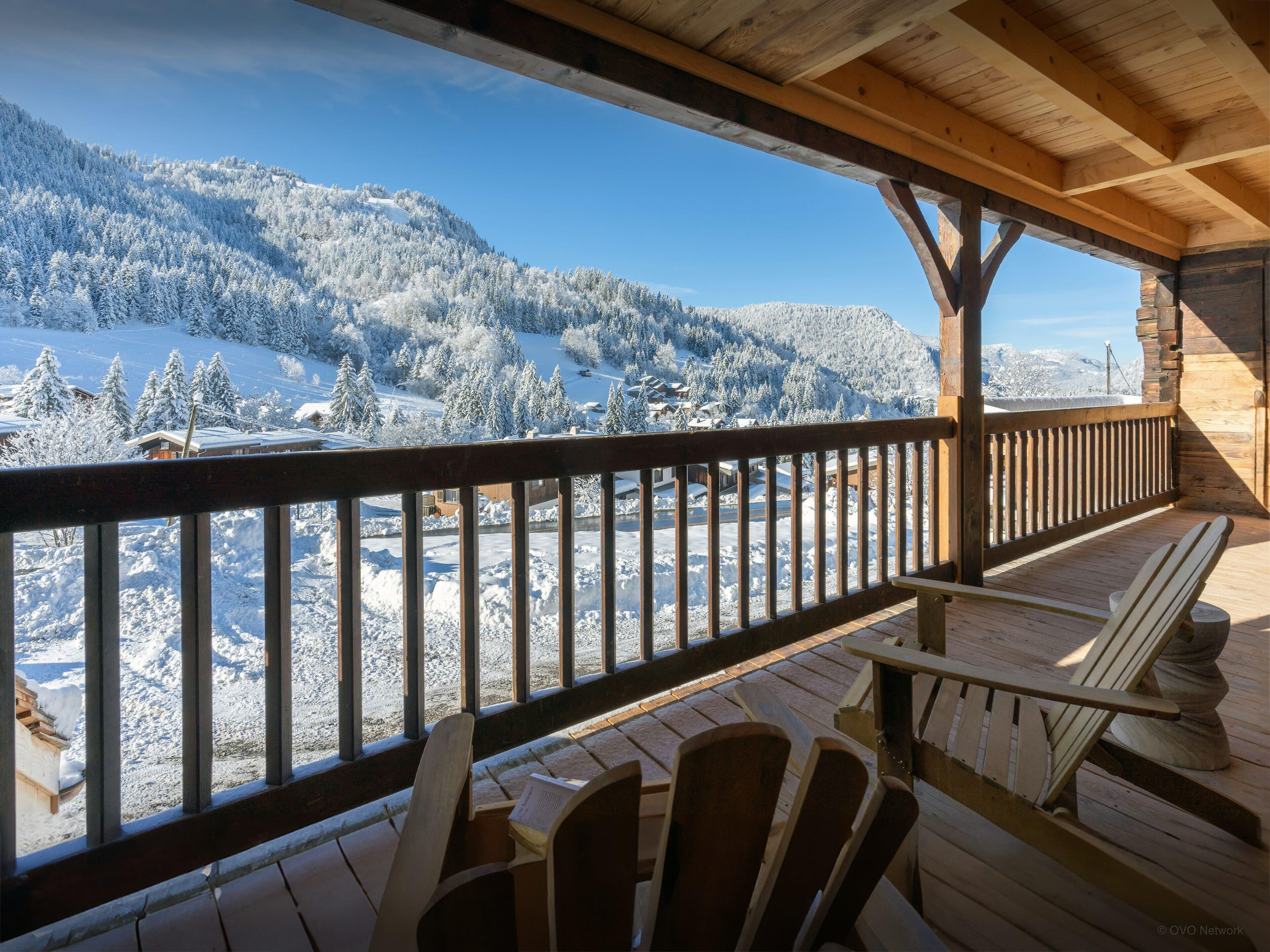 A wooden deck with chairs overlooking a snowy mountain landscape.