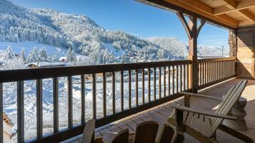 A wooden deck with chairs overlooking a snowy mountain landscape.
