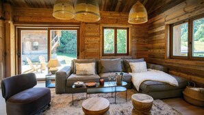 Ein gemütliches Blockhaus-Interieur mit einer Couch, einem Sessel und runden Holztischen.