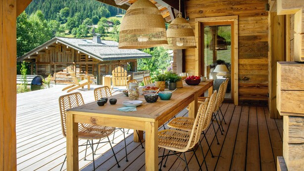 Eine Holzterrasse mit Esstisch, Korbstühle und hängenden Lampen aus Weidengeflecht.