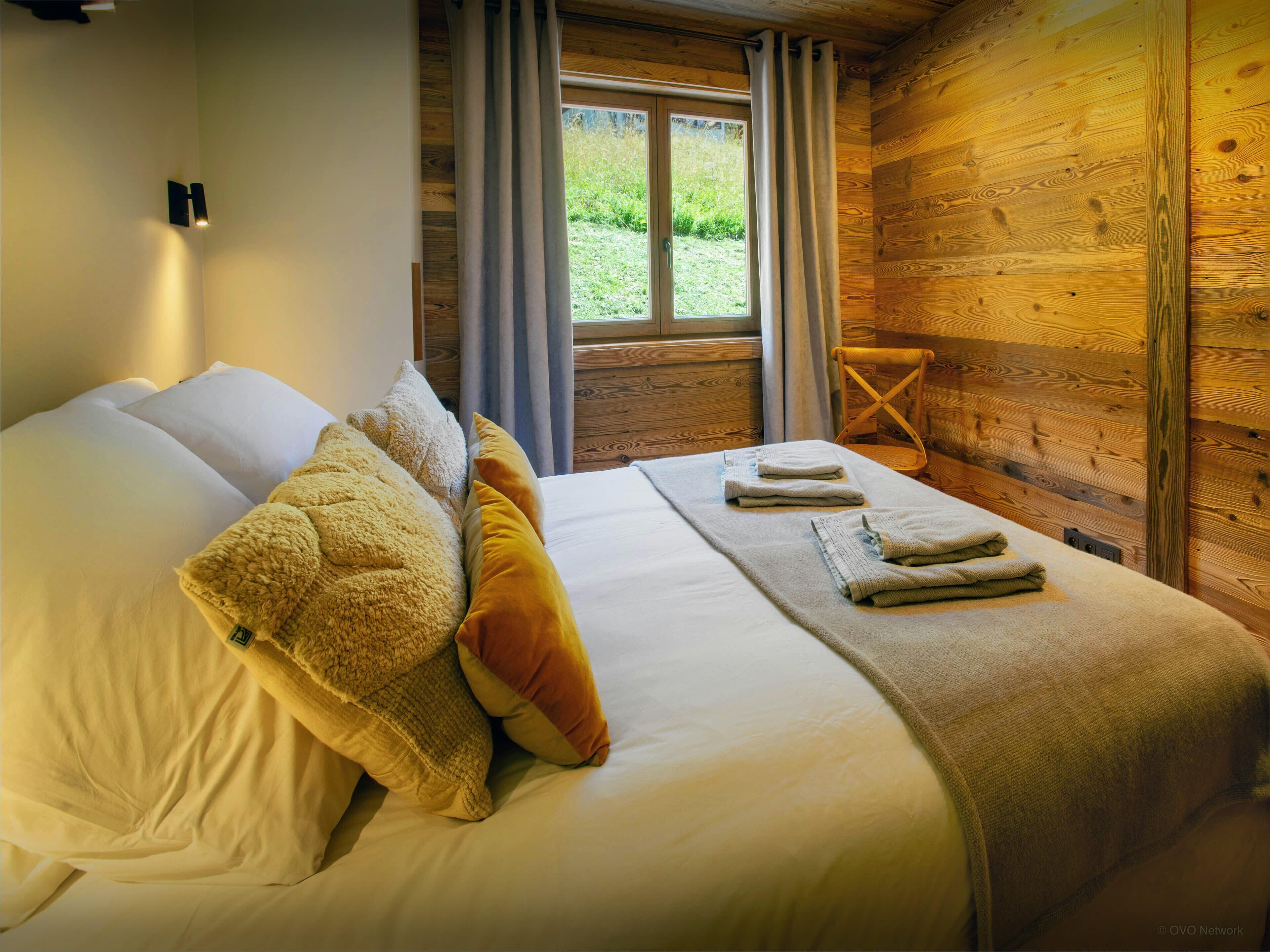 Une pièce de cabane en bois comprenant un lit, des oreillers et une fenêtre avec des rideaux.