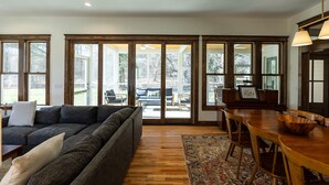 Una sala moderna con un sofá seccional gris oscuro, una mesa de comedor de madera y un amplio ventanal con vistas al exterior.