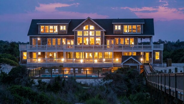 A large, multi-story beachfront house with a swimming pool, multiple balconies, and a wooden deck. - Hemingway & Mark Twain Estate | Weddings & Events | 32BR Sleeps 72 | OBX (Corolla)