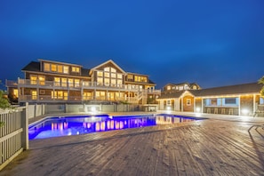 A large, multi-story house with a swimming pool and wooden deck. - Hemingway & Mark Twain Estate | Weddings & Events | 32BR Sleeps 72 | OBX (Corolla)