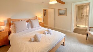 Een net opgemaakt bed met witte lakens en handdoeken, een houten hoofdbord en een nachtkastje met een lamp.