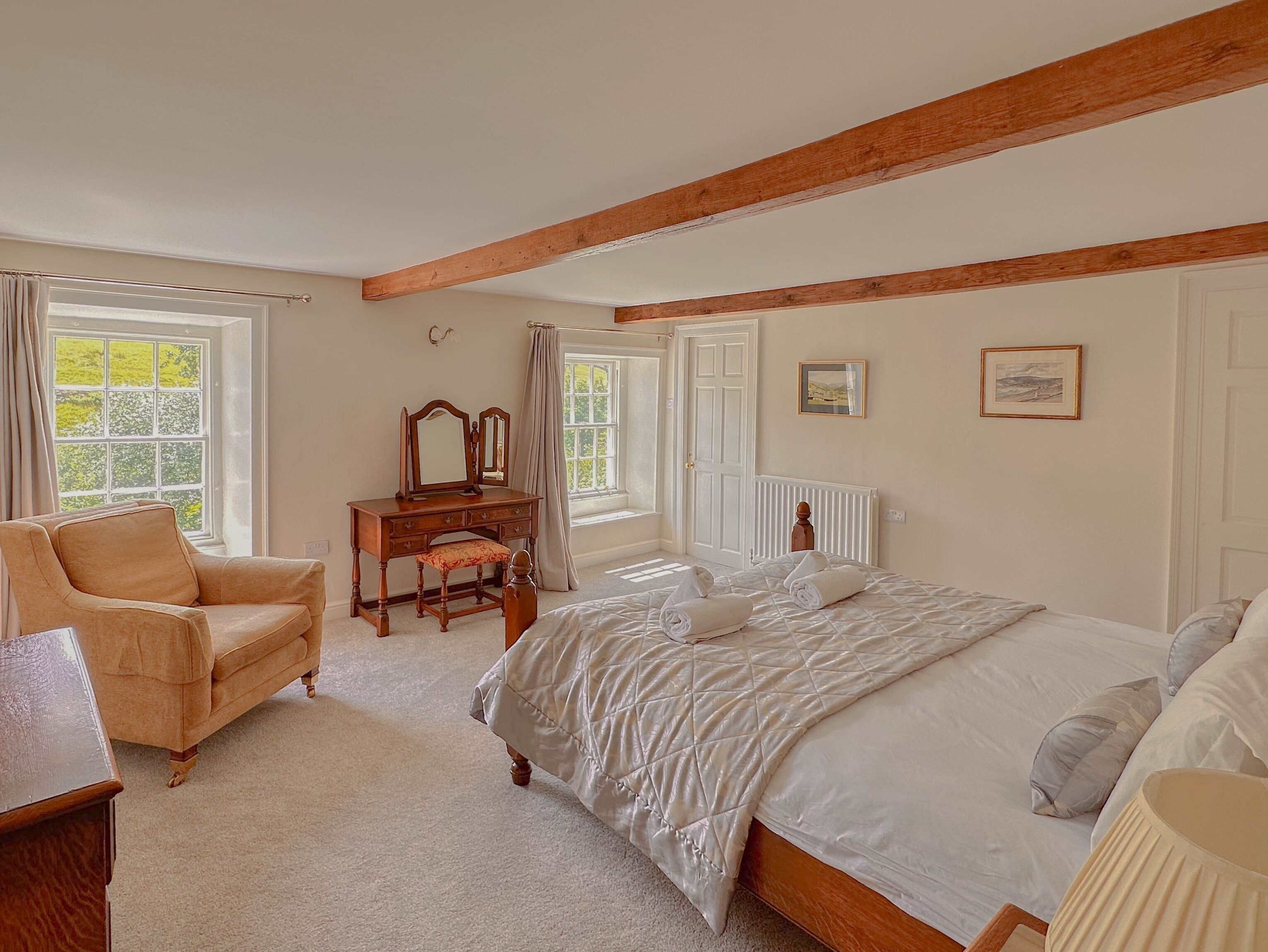 Une chambre à coucher avec un lit, une commode en bois, une chaise et une fenêtre avec des rideaux.