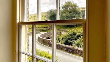 A window with a view of a stone wall, greenery, and a clear sky.