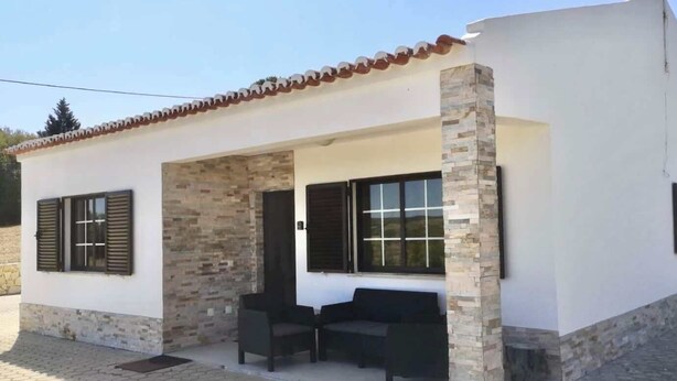 Un pequeño edificio con tejado de baldosas, paredes de piedra y un patio cubierto con mobiliario exterior.