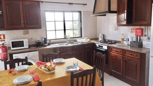 Una cocina con armarios de madera, una mesa de comedor para dos personas y un ventanal que deja entrar luz natural.