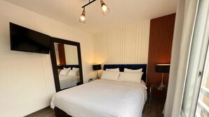 A hotel room with a large bed, a flat-screen TV mounted on the wall, and a wooden floor. - Apartamento DE 2 Dormitorios , A 4 Cuadras DEL Parque Kennedy (Miraflores)