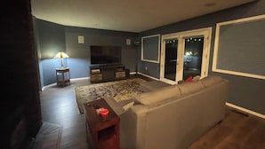 Un salon comprenant un canapé, un téléviseur, une lampe et une porte-fenêtre coulissante donnant sur un balcon.