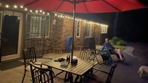 Une terrasse extérieure avec un parasol rouge, un mur en briques et des guirlandes lumineuses.