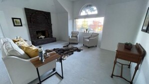 Un salon avec une cheminée, des canapés blancs, une table basse et une vue par la fenêtre.