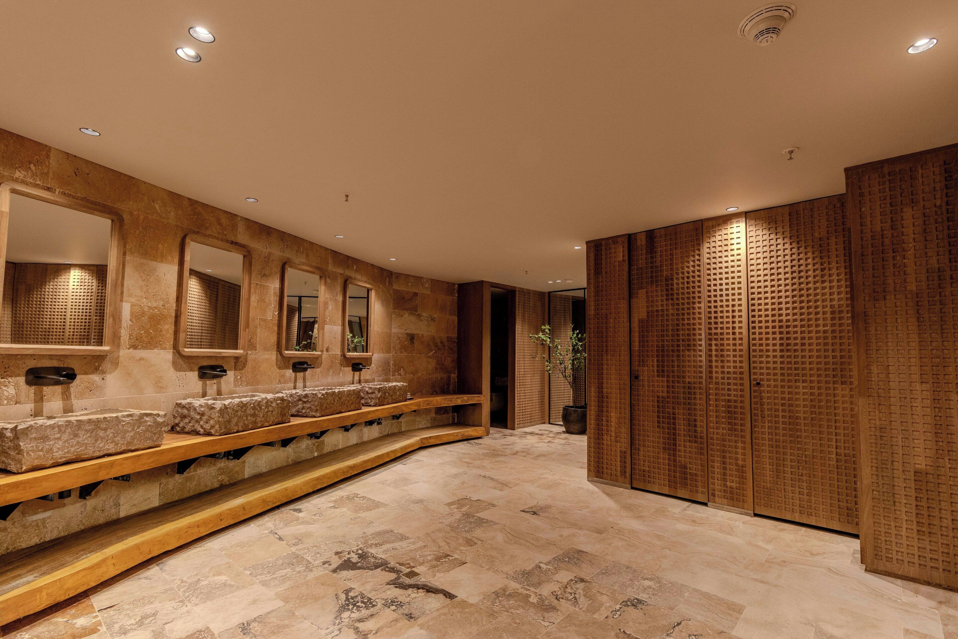 A modern bathroom with stone sinks, mirrors, and a wooden panel wall.