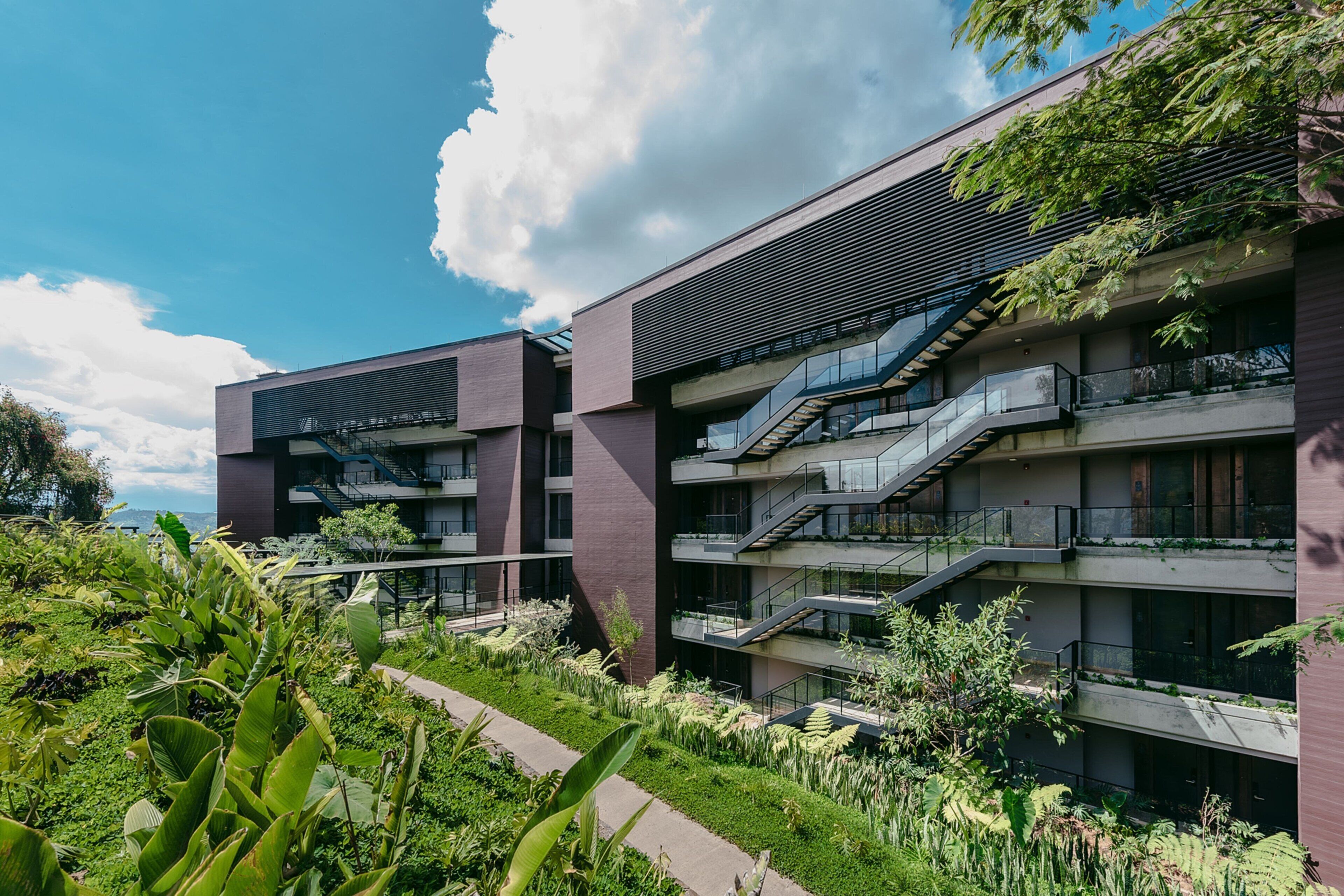A modern multi-story building with balconies and a garden area.