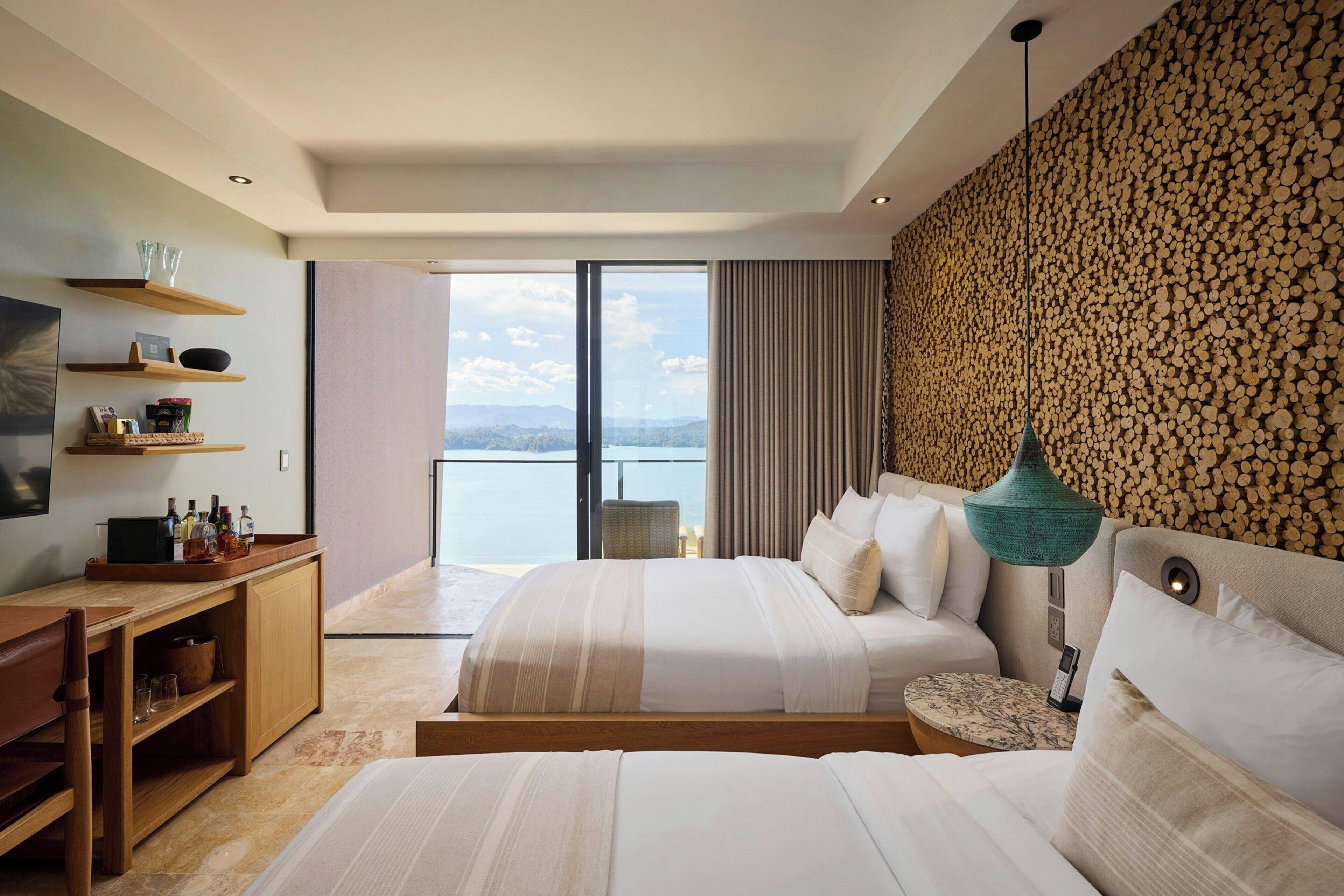 A modern hotel room with a large bed, a desk with a chair, and a view of the sea.