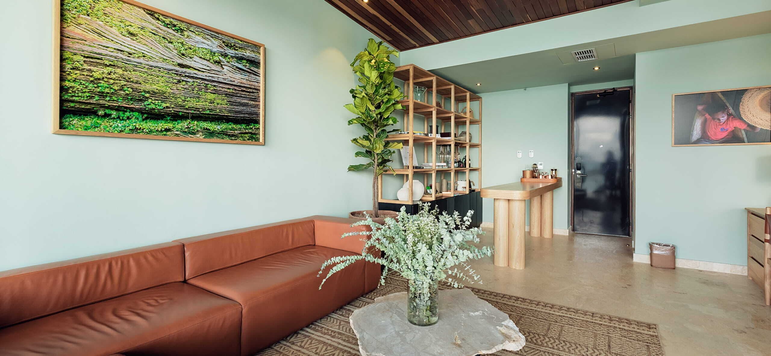 A modern living room with a brown leather sofa, a coffee table with a vase of flowers, a wooden bookshelf, and a large painting on the wall.