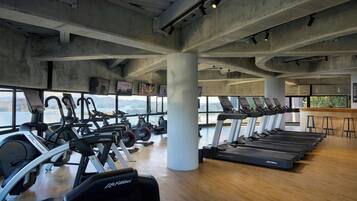 Un gimnasio con equipo cardiovascular, ventanas amplias y suelo de madera.