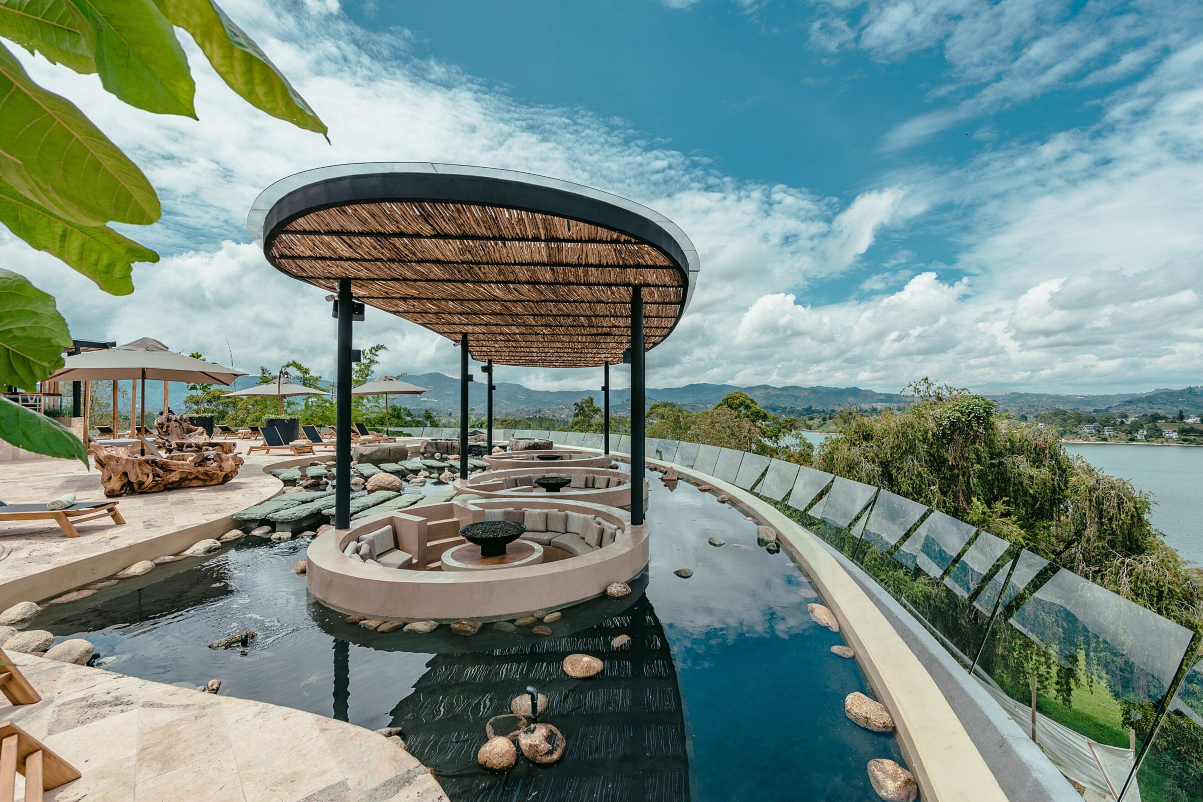 A pool area with a circular seating arrangement, a covered seating area, and a view of the surrounding landscape.