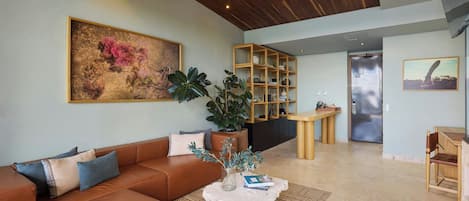 Un soggiorno moderno con un divano in pelle marrone, un tavolino da caffè con oggetti decorativi, una grande pianta in vaso e una libreria in legno.