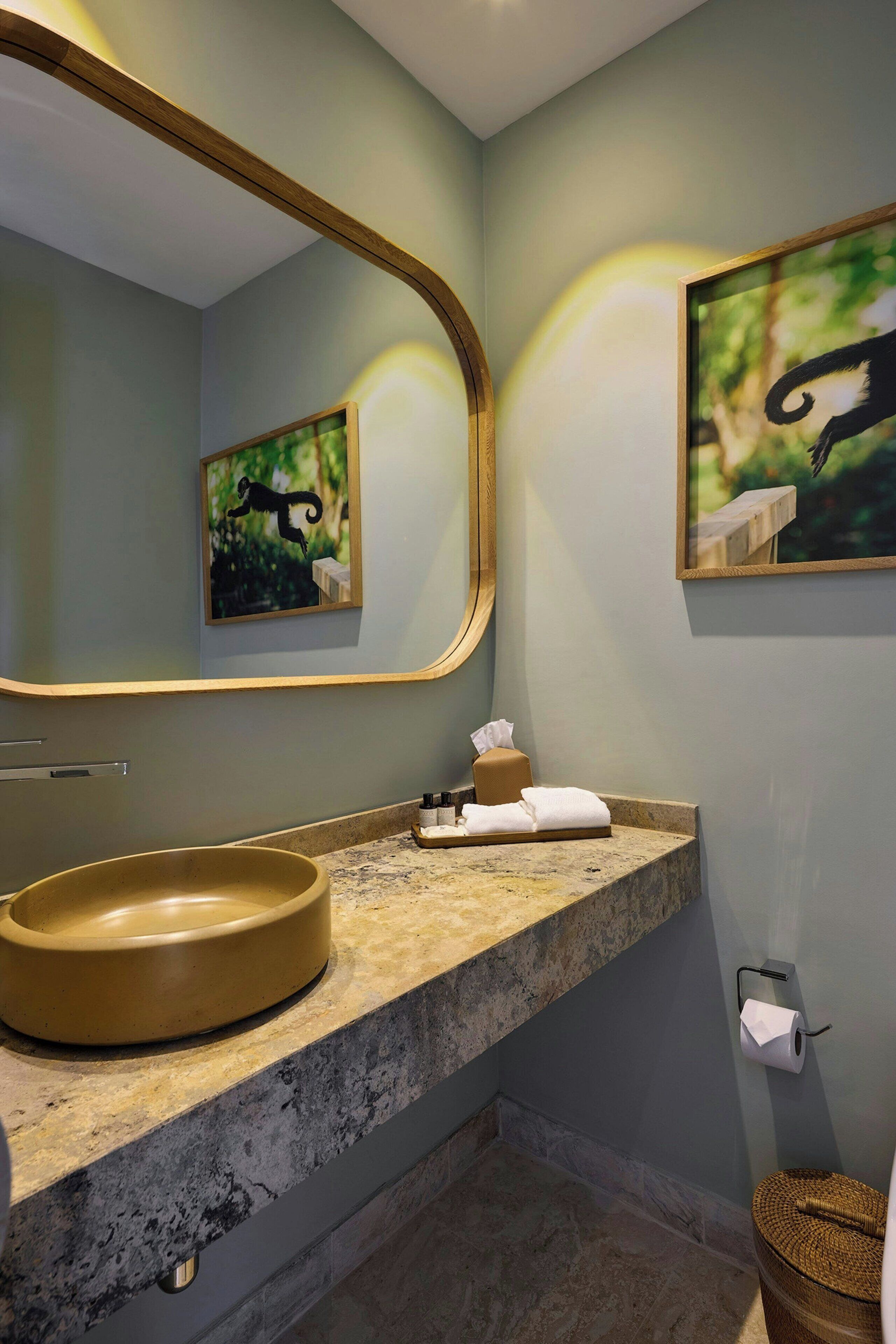 A bathroom with a large mirror, a round sink, and two framed pictures on the wall.
