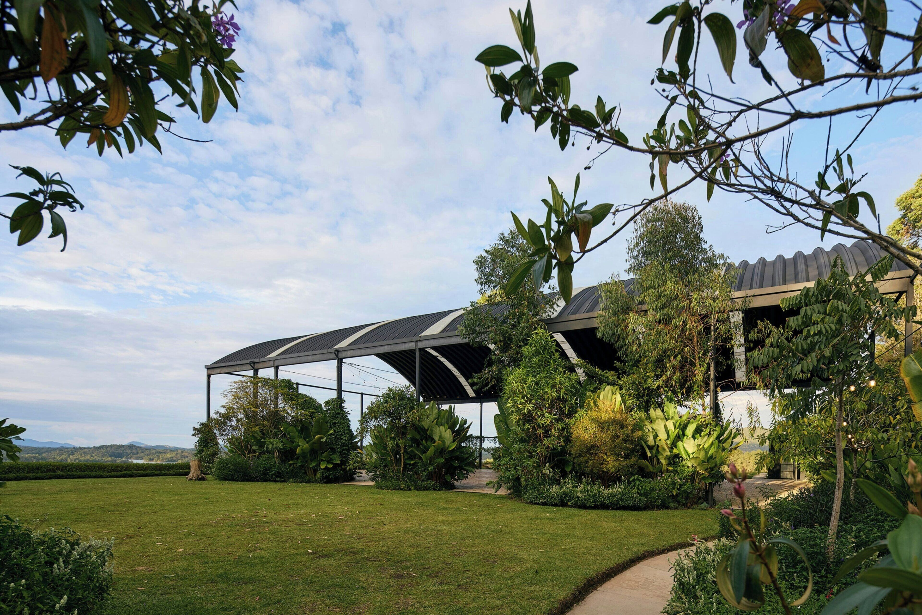 A modern building with a covered outdoor area, surrounded by lush greenery and a well-maintained lawn.